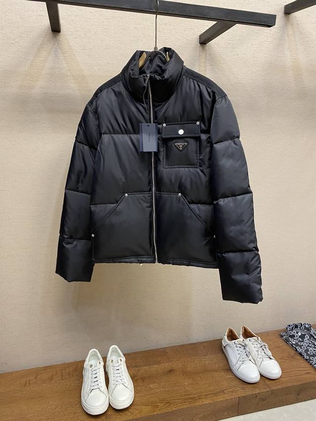 Prada、尼龙徽标羽绒夹克 Re-Nylon短款羽绒夹克采用环保的re-Nylon材料，这种材料的使用减少了对新资源的需求，降低了环境污染。面料密度非常高 抗